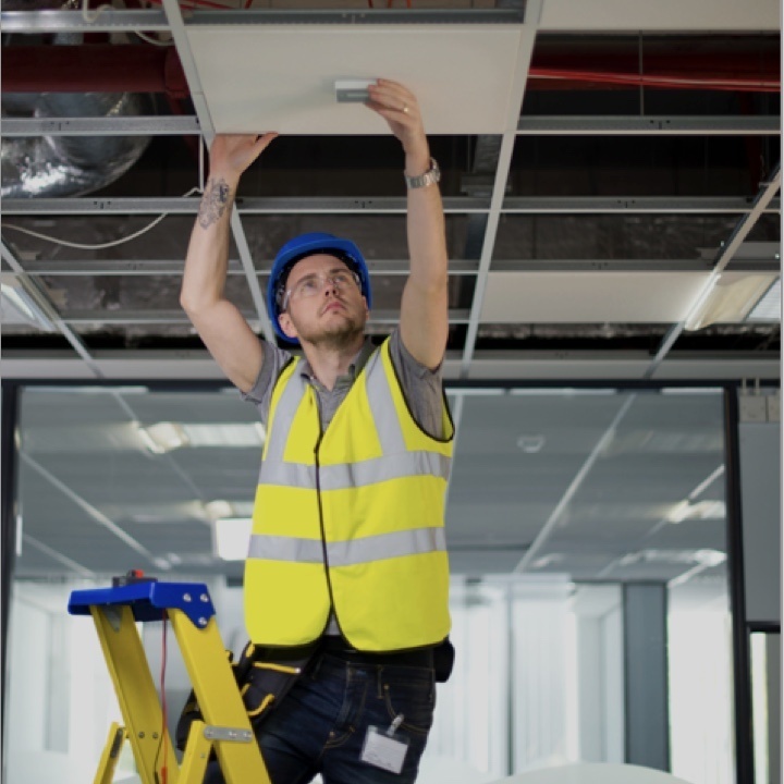 Man in construction vest and goggles installing a product in a ceiling