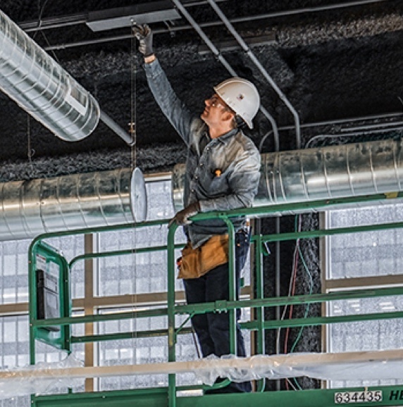 Building inspector on a step ladder looking at the ceiling in an industrial building